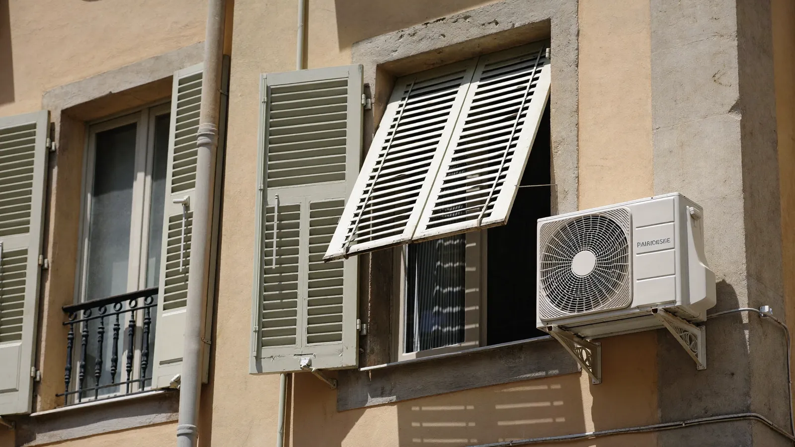Façade méditerranéenne aux volets bleu pâle avec une unité extérieure de climatisation, sous le soleil d'été marseillais